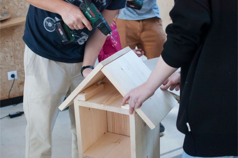 Zdjęcie przedstawia grupę uczestników warszatu pracujących nad domkiem dla zapylaczy