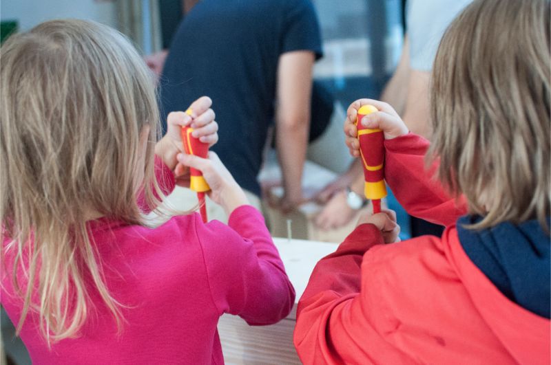 Zdjęcie przedstawia dwoje dzieci od tyłu, które trzymają śrubokręt w dłoniach. 