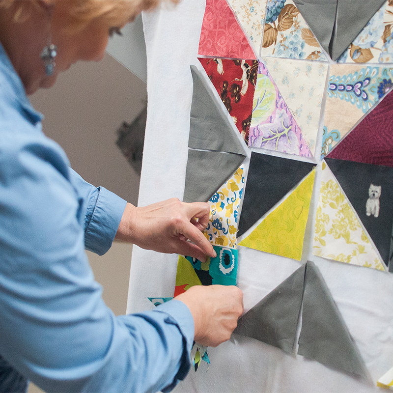 Zdjęcie przedstawia kobietę projektującą patchwork z kawałków tkaniny