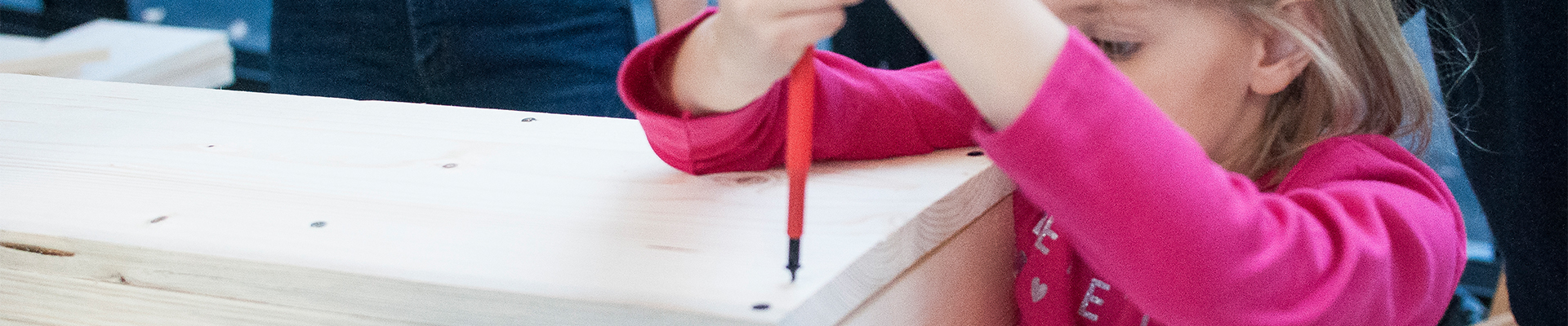 Zdjęcie przedstawia bliżej niezidentyfikowaną dziewczynkę, która przykręca śrubki do budowanego domku dla zapylaczy