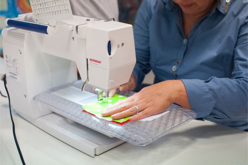 Zdjęcie przedstawia maszynę do szycia oraz dłonie szyjącej kobiety.