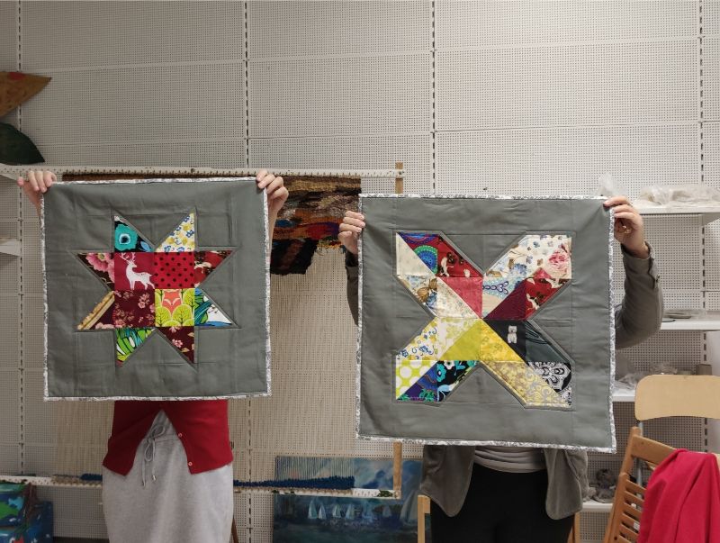 Zdjęcie przedstawia dwie postaci zasłaniające twarze swoimi pracami 