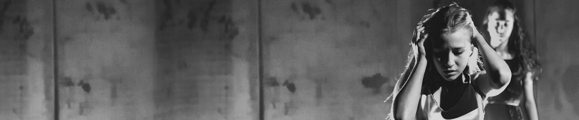 Na czarno białym zdjęciu pół portret tancerki. Tancerka trzyma ręce na głowie. W tle znajduje się druga tancerka.