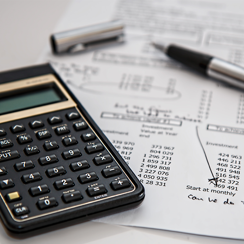 Na zdjęciu leżące na biurku wydrukowane kartki z tabelami, kalkulator oraz długopis